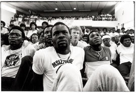 A man wearing aMsizi Dube T-shirt listens to speakers at a UDF rally