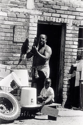 Black migrant worker  with his child at a (men-only) hostel for migrant workers in Crossroads