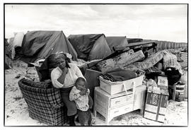 Woman and child with their furniture in front of long row of tents in Brown's Farm, Khayelitsha